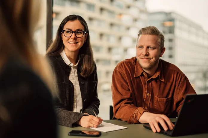 Två medarbetare står med ryggen mot fönster och lyssnar på en kollega