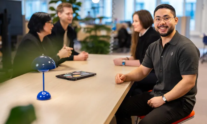 Medarbetare på Axfood sitter vid ett bord, ler mot kameran