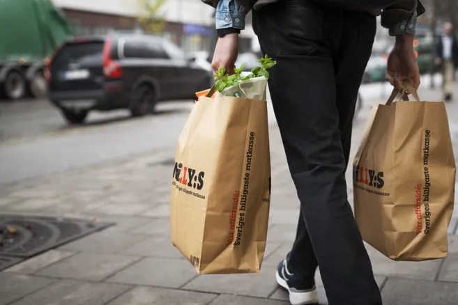 En person går mot en parkerad bil med två Willys kassar i handen